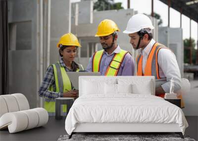 Team of construction engineers wearing vest and helmet safety discussing project at construction site. Group Indian foreman with laptop, paperwork working at factory making precast concrete wall. Wall mural