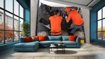 Top view of two mechanic men wearing orange shirt checking and repairing engine of car under hood car at auto service garage Wall mural