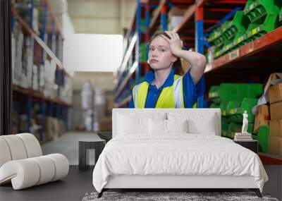 Woman warehouse worker feeling confused and failed to check inventory stock mistake while working in warehouse factory store. Stressed young girl employee with tablet holding her head unhappy. Wall mural