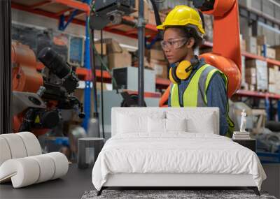 Young African American female engineer with tablet operating welding robot arm machine in warehouse factory.Professional technician automation robotic industrial Wall mural