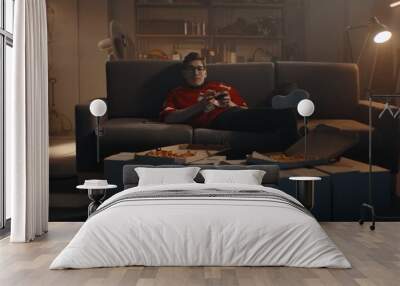 POV Portrait of Caucasian teenager playing video game inside home garage, enjoying pizza. Shot with 2x anamorphic lens Wall mural