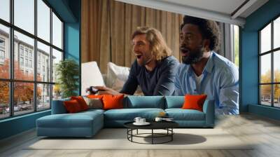 Two 30s male friends - African-American and Caucasian, playing video games at home, laughing and having fun Wall mural