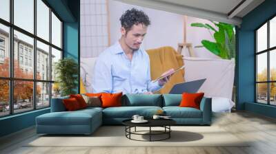 Businessman smiling sitting on home house indoor modern sofa using laptop technology, entrepreneur adult man male person using wireless internet connection working notebook in business communication Wall mural