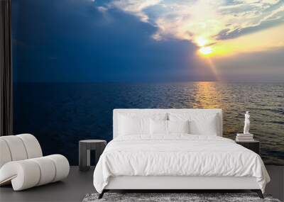 Blue ocean with sun rays coming through the clouds during sunrise or sunset. Calm waters in vast sea reflecting golden sunlight. Symbolic photo of hope and calmness. Wall mural