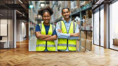 Asian male and African American female employees wearing colleague uniforms standing with their arms crossed and proud of warehouse and freight service. Wall mural