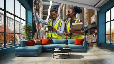 female African American employee and an Asian employee wearing a uniform holding tablet and working together to inspect goods in the warehouse.
 Wall mural