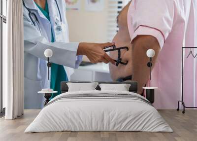 Nutritionist hand using measuring body fat with caliper device to measure belly of obese elderly male patient for obesity treatment and dieting in hospital Wall mural