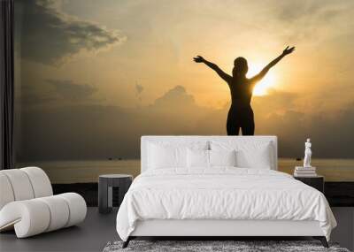 Silhouette of Asian girls stand with arms raised to feel free  and enjoying  life on the beach at sunrise  in morning .Freedom  and Wellbeing concept. Wall mural