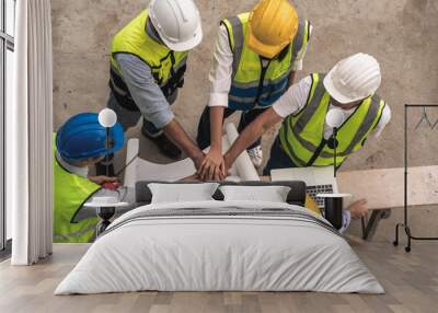 team of male and female engineers and contractors look at blueprints and join hand together at the construction site. Teamwork concept. Wall mural