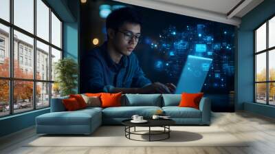 A young man wearing glasses is sitting in front of a laptop computer. The background is dimly lit, and there are glowing technology lines in the background Wall mural