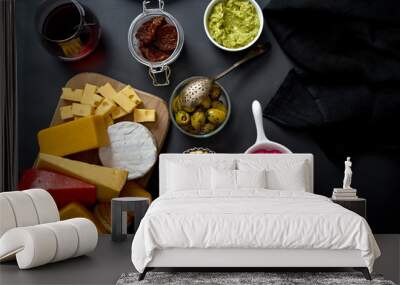 Wooden board with various types of cheese and snacks and two glasses of red wine on black table Wall mural