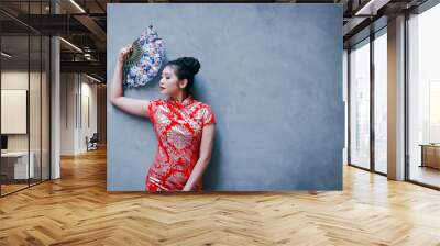 Young woman wearing red Chinese dress Welcome the new year Holding a blue fan The background is a plaster wall. Have space to write messages Wall mural