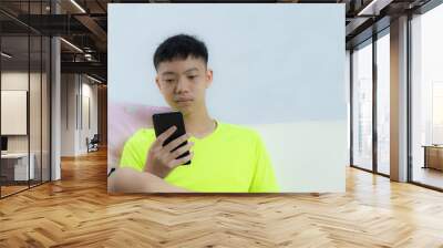 a young black-haired asian man holds a smartphone in his right hand. and staring at the smartphone.  Wall mural