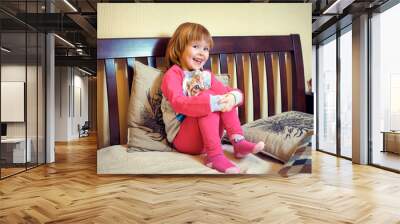 A small child in pink pajamas is sitting on the bed Wall mural