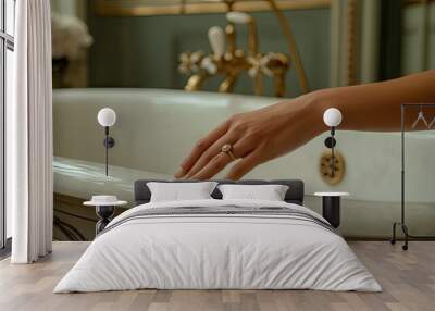 A close-up of a womans hand wearing a gold ring, resting on the rim of a vintage-style bathtub, evoking elegance and luxury. Wall mural