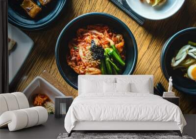 A vibrant bowl of kimchi made with cabbage, sitting next to other traditional Korean side dishes, all neatly arranged on a wooden table. Wall mural