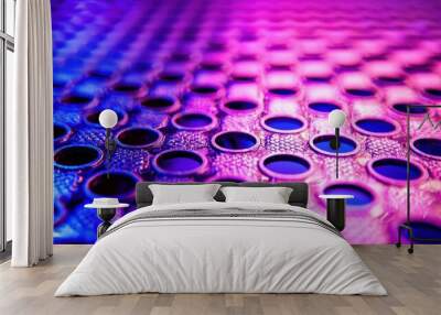 Close-up view of a vibrant patterned surface with circular holes, illuminated by colorful lights, creating an abstract design. Wall mural