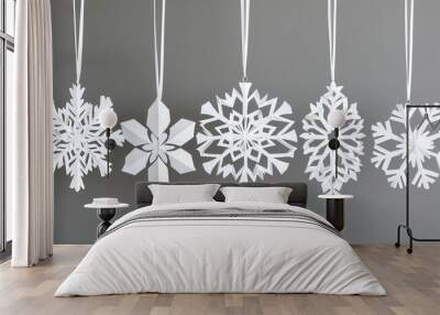 Elegant white paper snowflakes hanging against a gray background, perfect for winter decorations and holiday themes. Wall mural