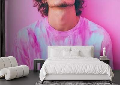 Young man with curly hair poses confidently in a vibrant pink tie-dye shirt against a colorful backdrop. Wall mural