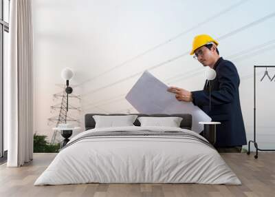 An engineer wear yellow hard hat and suite hold blueprint in hand standing on field looking at blueprint Wall mural