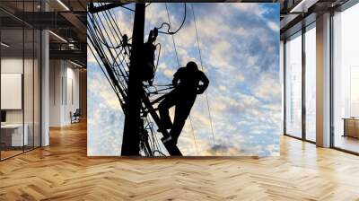 Silhouetted electricians working at electric pole in blue sky background. Wall mural