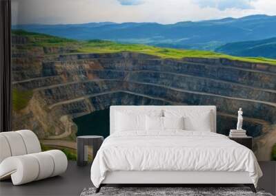 A breathtaking view of a large open-pit mine surrounded by lush green hills and a serene lake under a bright blue sky. Wall mural