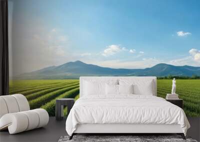 A scenic landscape featuring lush green fields under a bright blue sky with mountains in the background and a warm sunlight. Wall mural