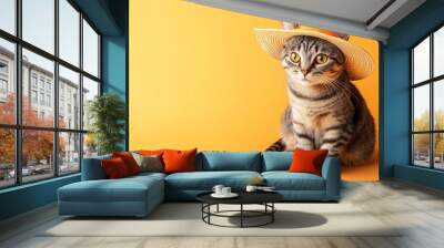 A cat wearing a straw hat poses against a vibrant orange background. Wall mural