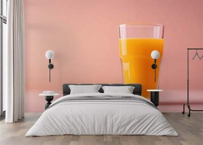 A clear glass filled with vibrant orange juice against a soft pink background. Wall mural