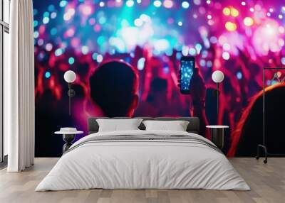 A crowd at a concert with colorful lights, capturing the moment on a smartphone. Wall mural