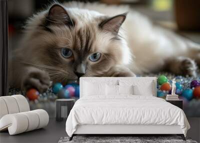 A fluffy cat curiously plays with colorful marbles on a textured surface. Wall mural