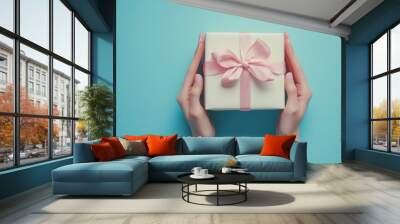 A gift box held by hands against a blue background, symbolizing celebration and surprise. Wall mural