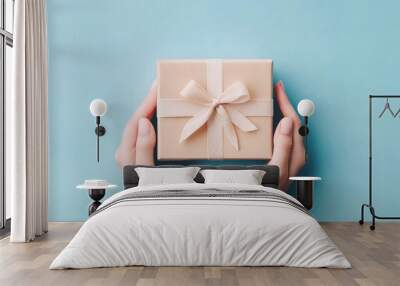 A pair of hands holding a beautifully wrapped gift box with a ribbon on a pastel background. Wall mural