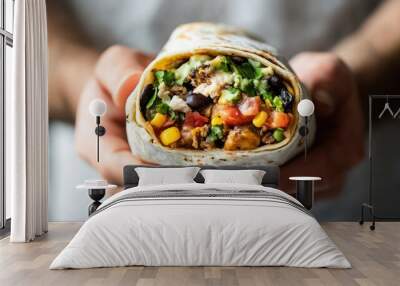 A person holds a delicious, colorful burrito filled with various ingredients. Wall mural