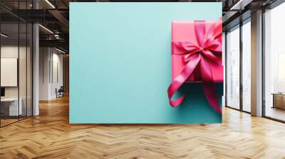 A pink gift box with a ribbon on a light blue background, symbolizing celebration and surprise. Wall mural