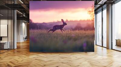 A rabbit leaps across a vibrant field at sunset, showcasing nature's beauty and tranquility. Wall mural