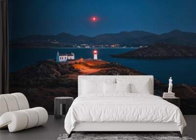 A serene lighthouse scene at dusk with a glowing red light and distant hills. Wall mural