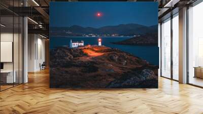 A serene lighthouse scene at dusk with a glowing red light and distant hills. Wall mural