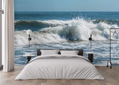 A serene view of ocean waves crashing on a shore under clear blue skies. Wall mural