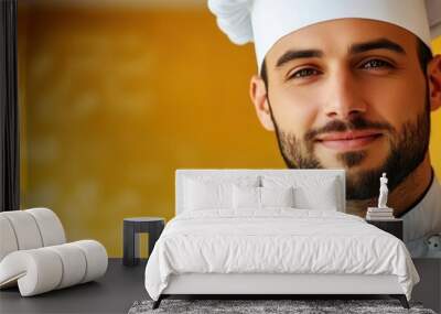 A smiling chef in a white uniform and hat stands against a yellow background. Wall mural