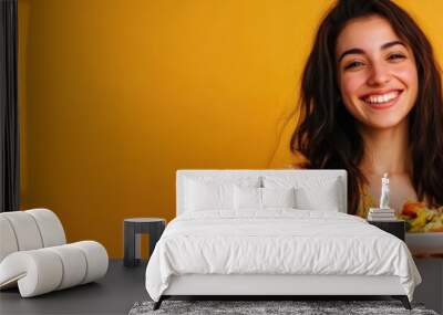 A smiling woman holds a colorful salad plate against a vibrant yellow background. Wall mural