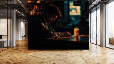 A solitary figure sits at a bar, reflecting in warm, dim light with a drink in front. Wall mural