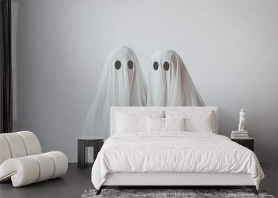 Two ghost figures in white sheets with black eyes against a plain background. Wall mural