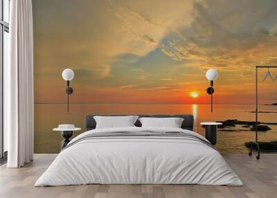 a beautiful sunset with rocks in the water and the setting sun Wall mural