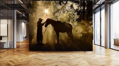 The silhouette of a cowboy man with his horse and sunshine in the morning Wall mural