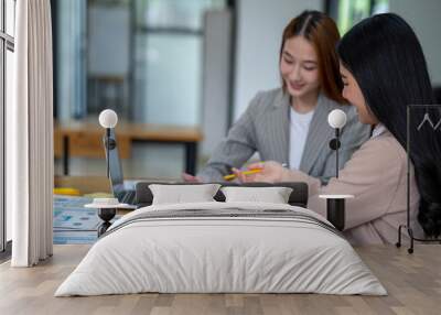 Two Asian businesswomen working Creative discussion in office using laptop and tablet, business concept Wall mural