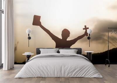 Human holding Bible book and christian cross with light sunset background Wall mural