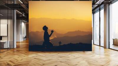 young man kneeling down and praying with christian cross at sunset background. christian silhouette  Wall mural