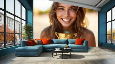 A cheerful young woman in stylish attire beams as she holds a contemporary vintage trophy, her smile and relaxed demeanor showcasing success. Wall mural