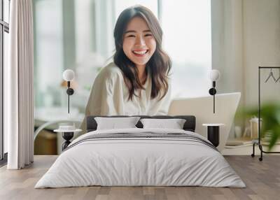 A Smiling Asian Woman working with her laptop in front of light cream background. generative AI. Wall mural